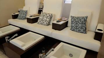 A hotel bathroom with multiple sinks, a sofa with patterned cushions, and a trash bin.