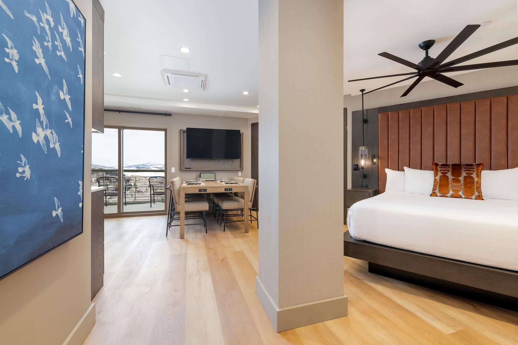 Habitación de hotel moderna con una cama grande, un escritorio con silla, televisión y un balcón con vistas.