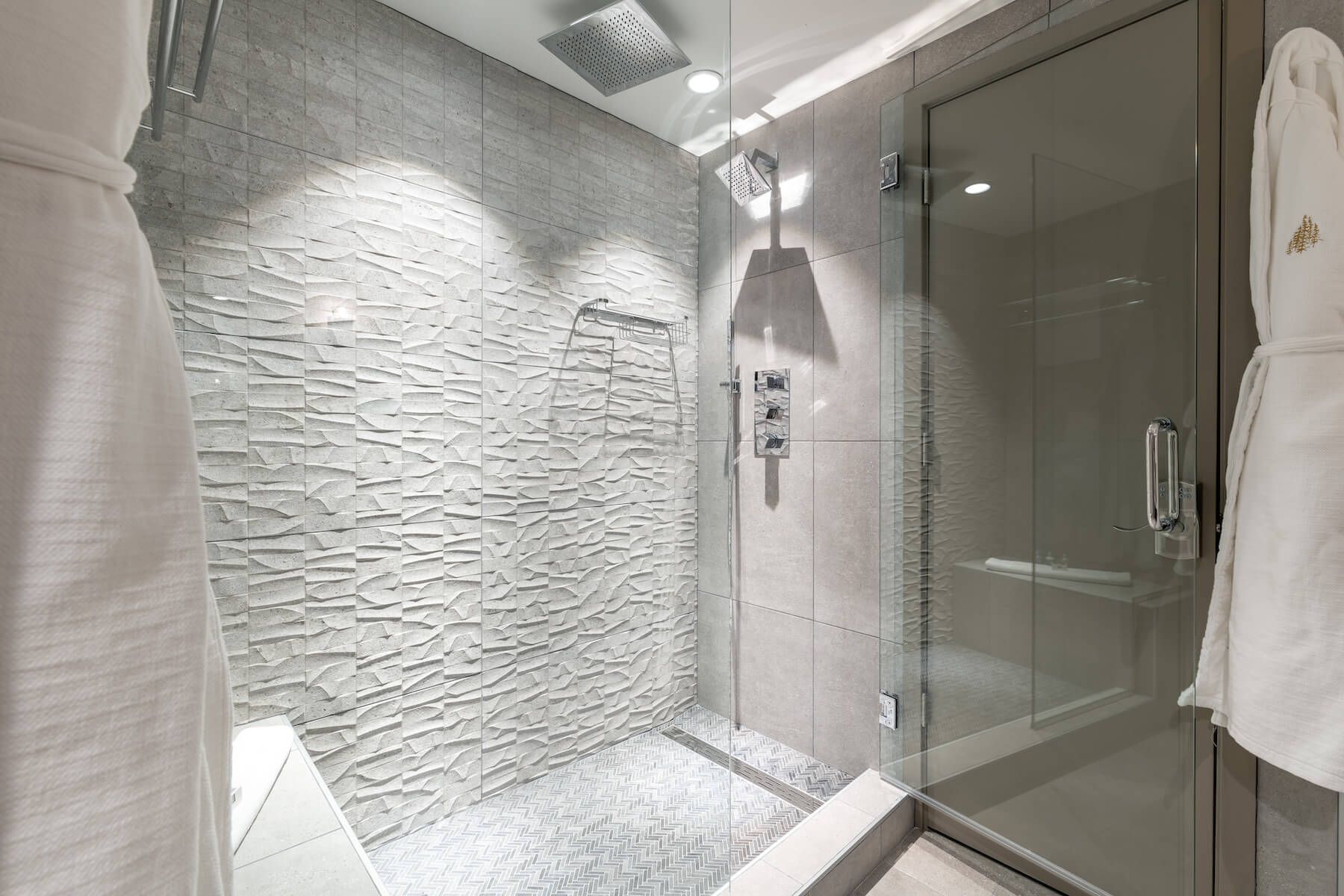 Une salle de bain moderne avec un mur à texture, une douche en verre et une serviette blanche accrochée à la porte.
