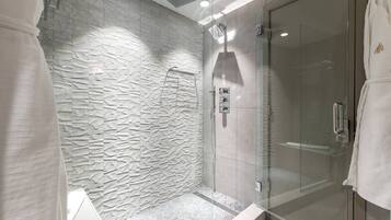 Une salle de bain moderne avec un mur à texture, une douche en verre et une serviette blanche accrochée à la porte.