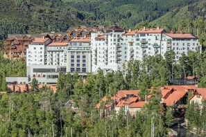 Hotel com vários andares e um pátio central, rodeado por árvores, com montanhas ao fundo.