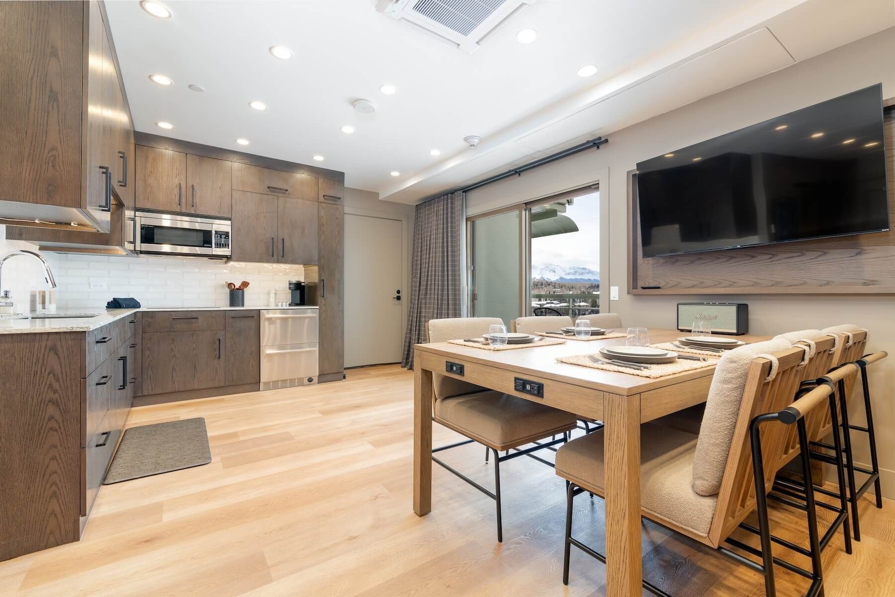 A modern kitchen with wooden cabinets, a built-in microwave, and a dining area with a table and chairs.