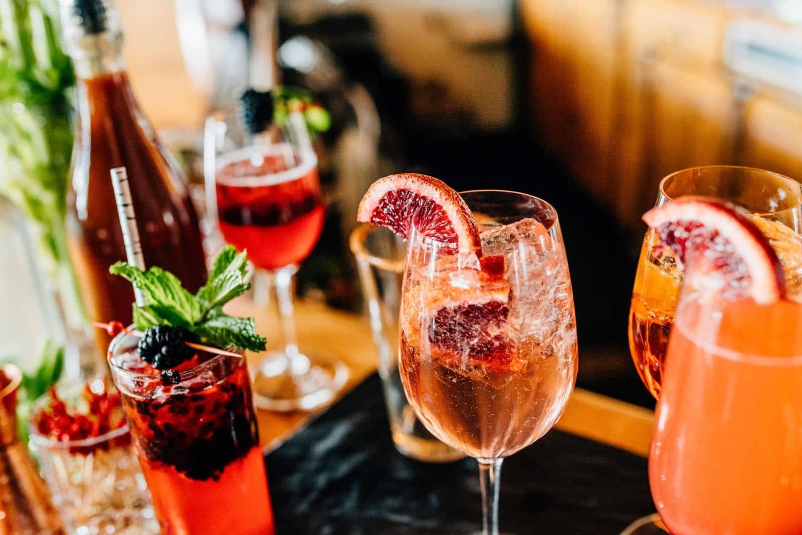 A variety of drinks with garnishes, including a glass with a slice of blood orange and mint leaves.