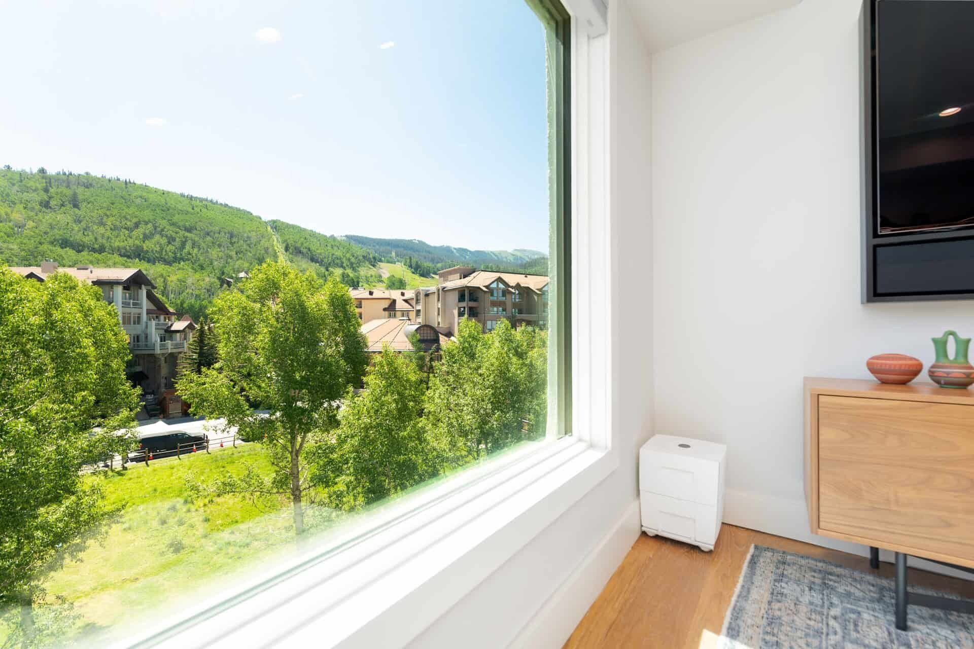 A room with a large window overlooking a mountainous landscape, a wooden cabinet, and a small white device on the floor.