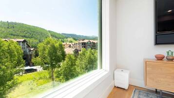 A room with a large window overlooking a mountainous landscape, a wooden cabinet, and a small white device on the floor.
