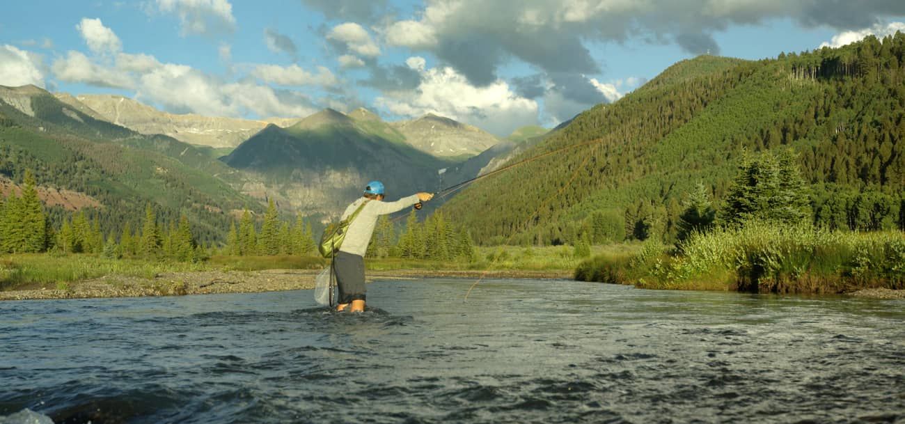 A person standing in a river with mountains in the background.