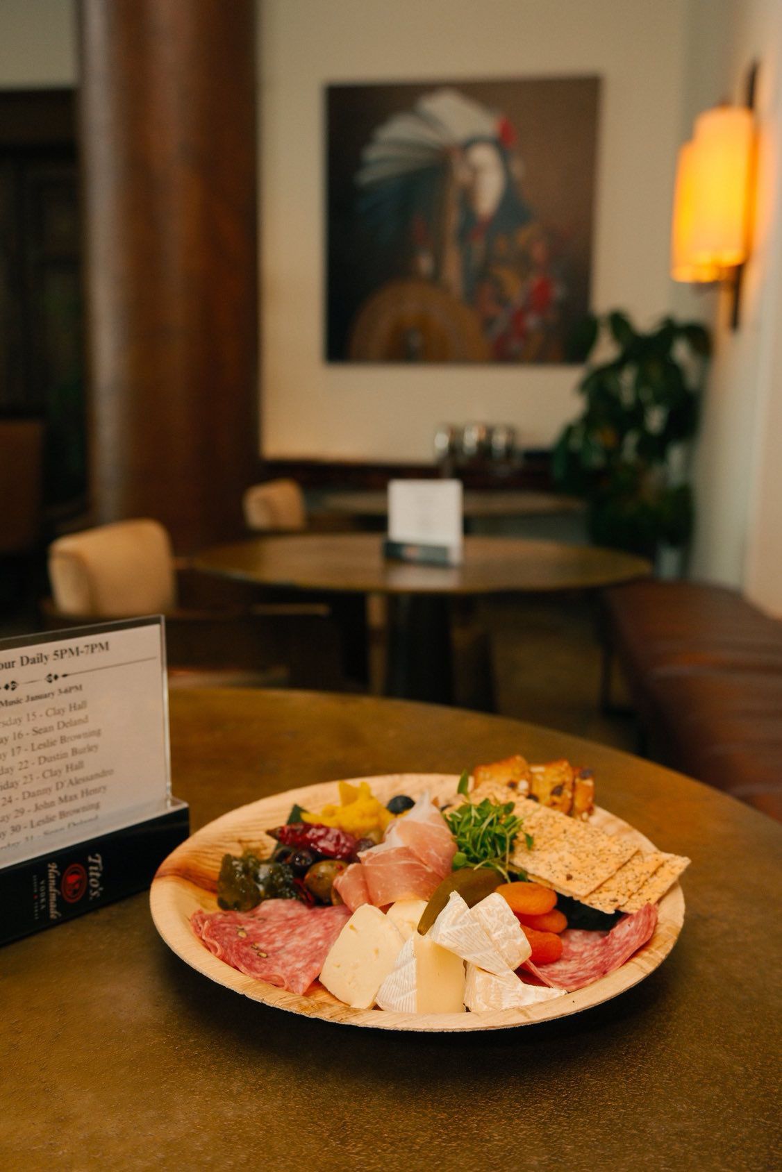 A wooden table with a charcuterie board featuring various meats, cheeses, and vegetables. A menu sign is visible in the foreground.