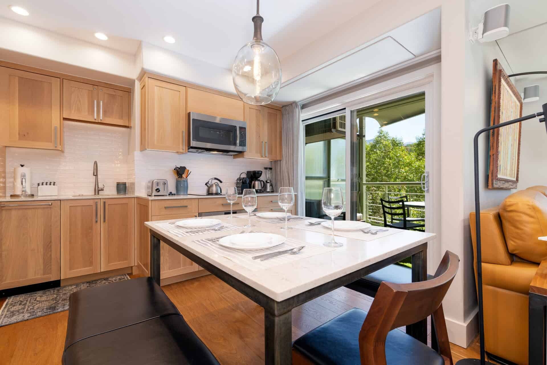 A modern kitchen with wooden cabinets, a central island with seating, and a dining area with a table set for four.