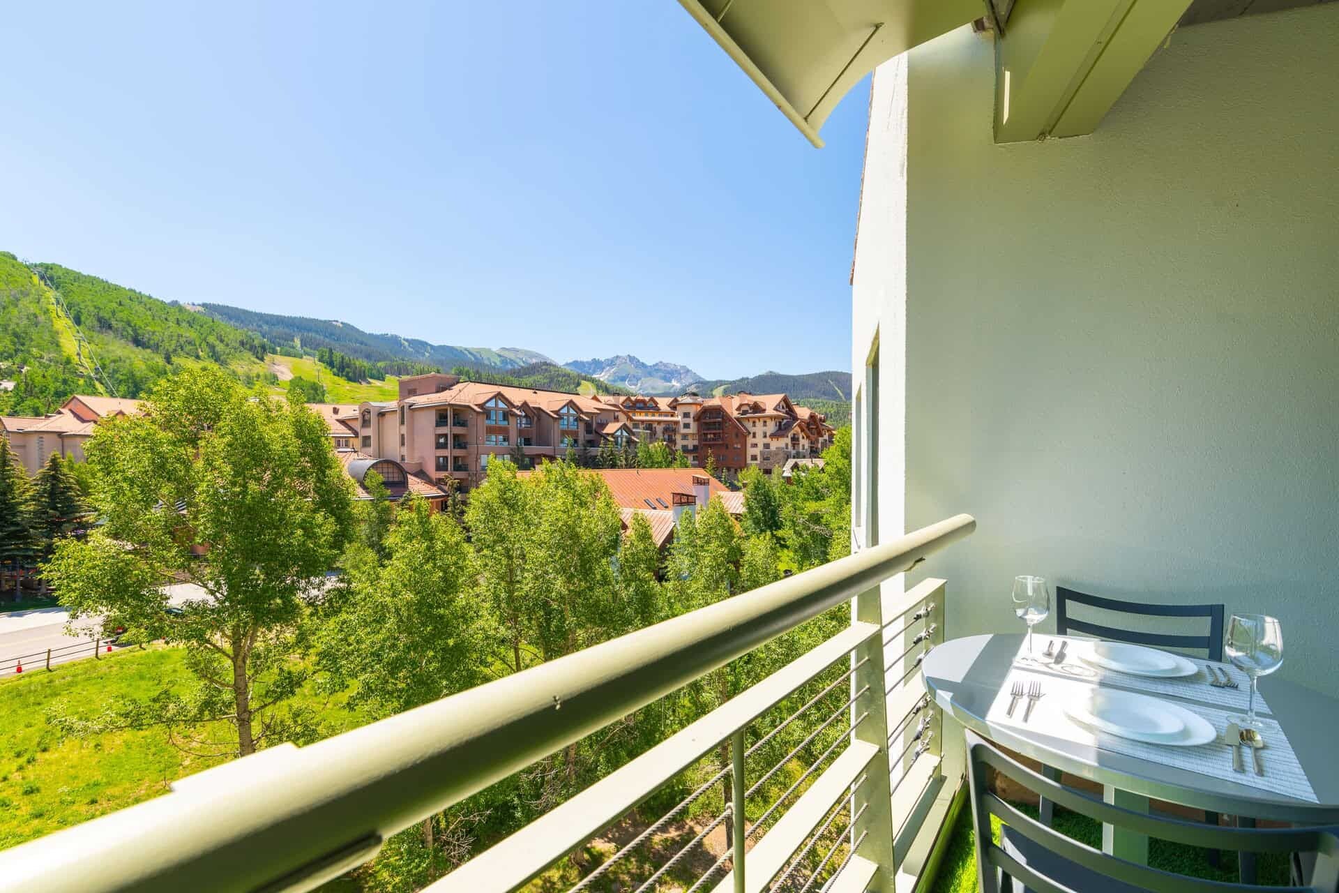 Un balcón con una mesa lista para comer, con vistas a una zona montañosa y edificios.