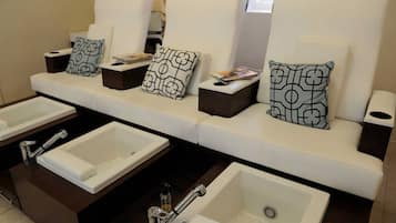 A hotel bathroom with multiple sinks, a sofa with patterned cushions, and a trash bin.
