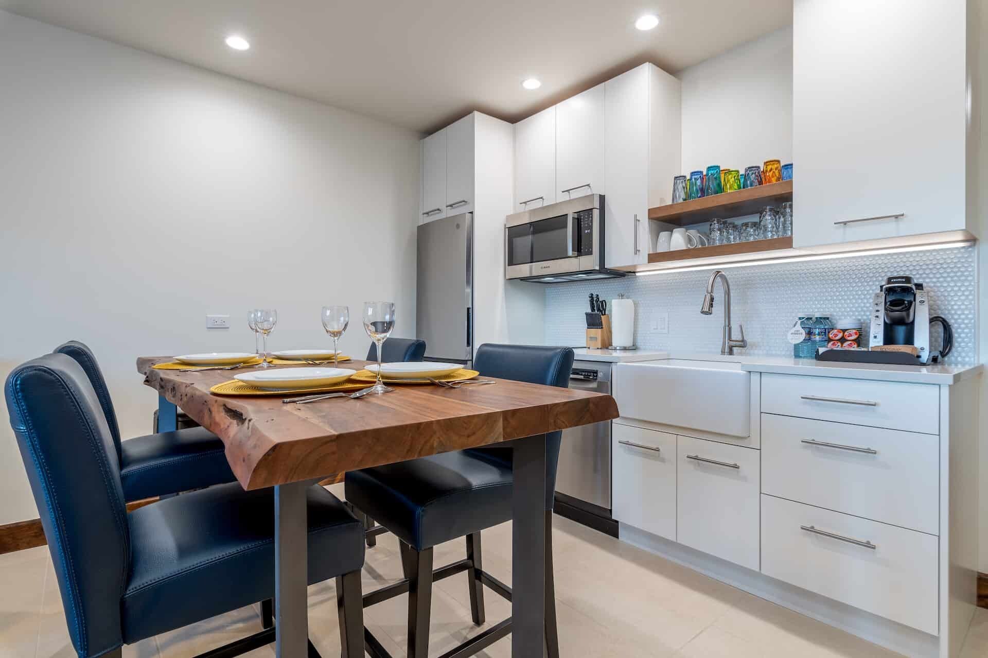 A modern kitchen with white cabinets, a wooden dining table, and blue chairs.