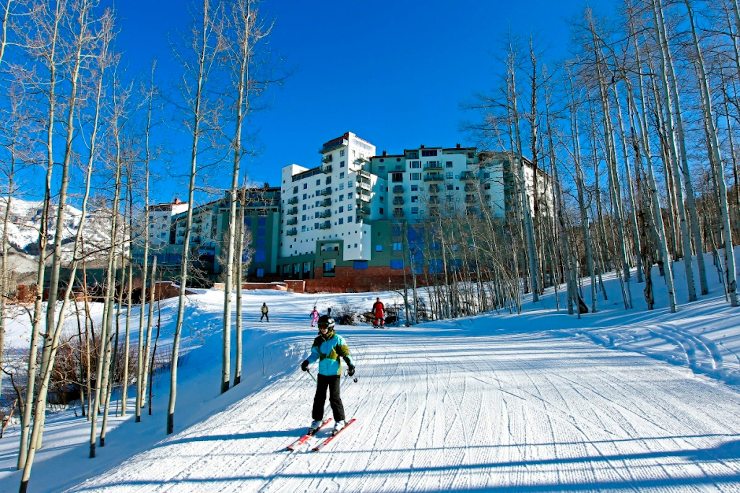 A ski resort with a large building in the background, surrounded by snow-covered trees.