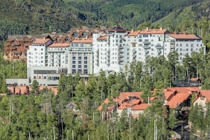A multi-story hotel with a central courtyard, surrounded by trees and set against a mountainous backdrop. - Ski-In/Ski-Out 1BR Suite w/ Mountain Views + Pools (Mountain Village)