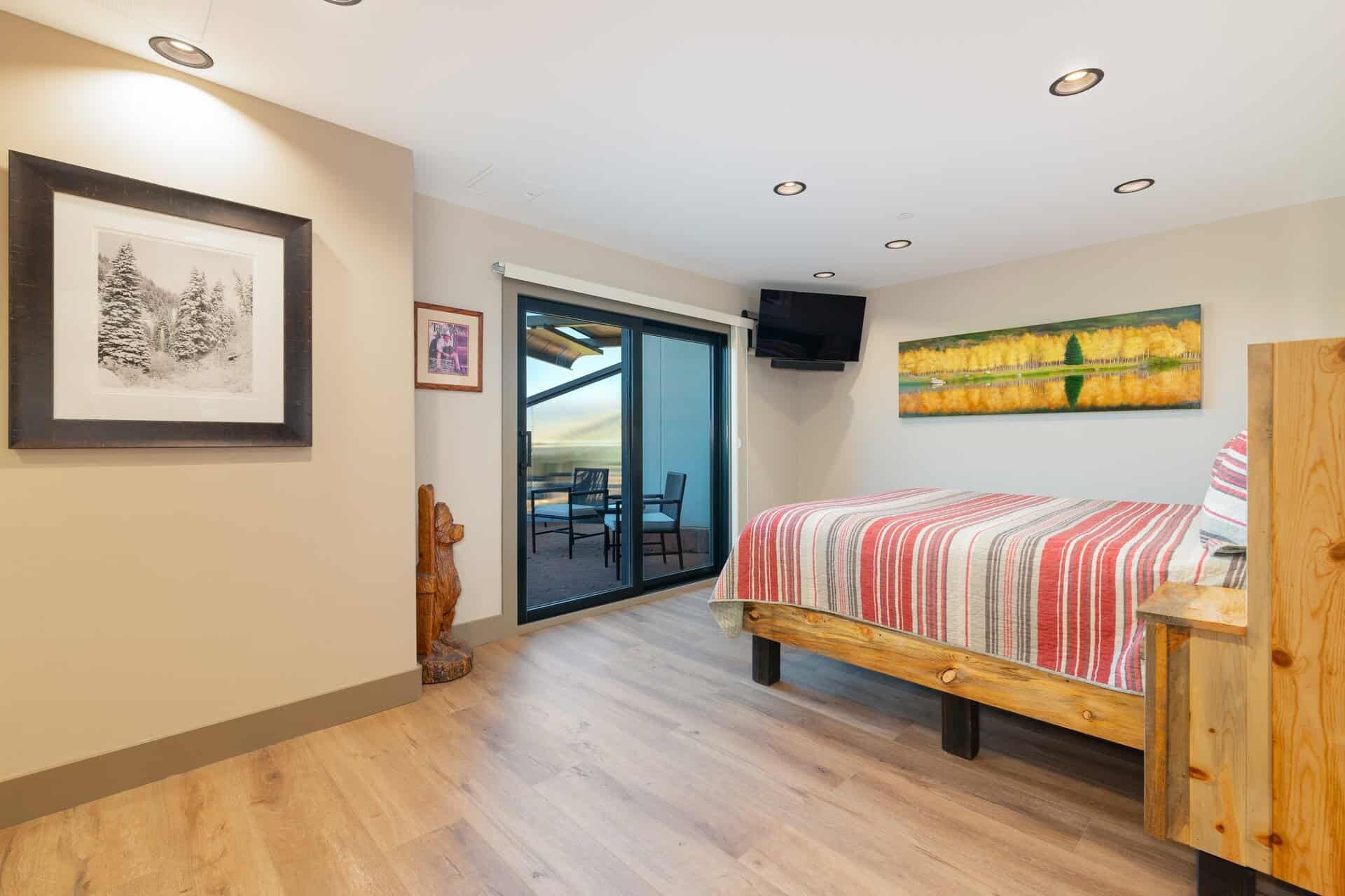 A bedroom with a bed, a wooden bench, a TV, and a painting.