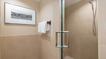 Una ducha con cerramiento de vidrio, ducha de mano, paredes con azulejos color beige y una fotografía blanco y negro enmarcada en la pared.