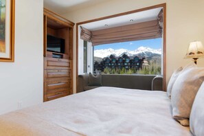 Quarto com cama, televisão, janela com vista para montanhas e abajur.