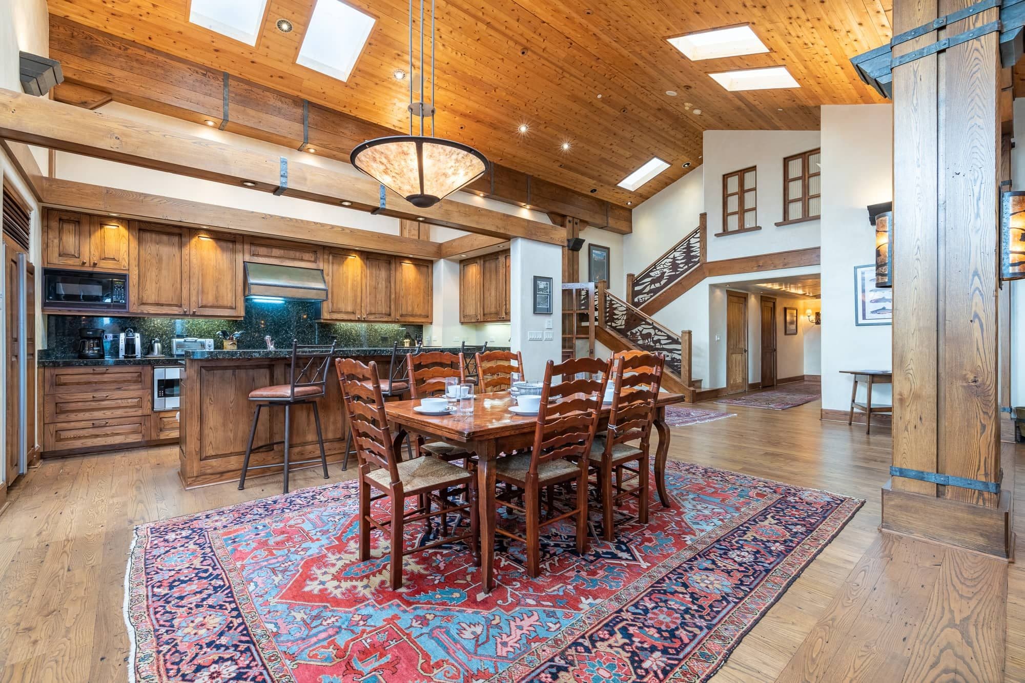 A spacious kitchen with wooden cabinets, a dining area with a large table and chairs, and a staircase leading to an upper level.