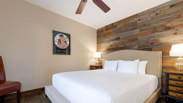 A hotel room with a large bed, a wooden accent wall, a framed picture on the wall, and a nightstand with a lamp.