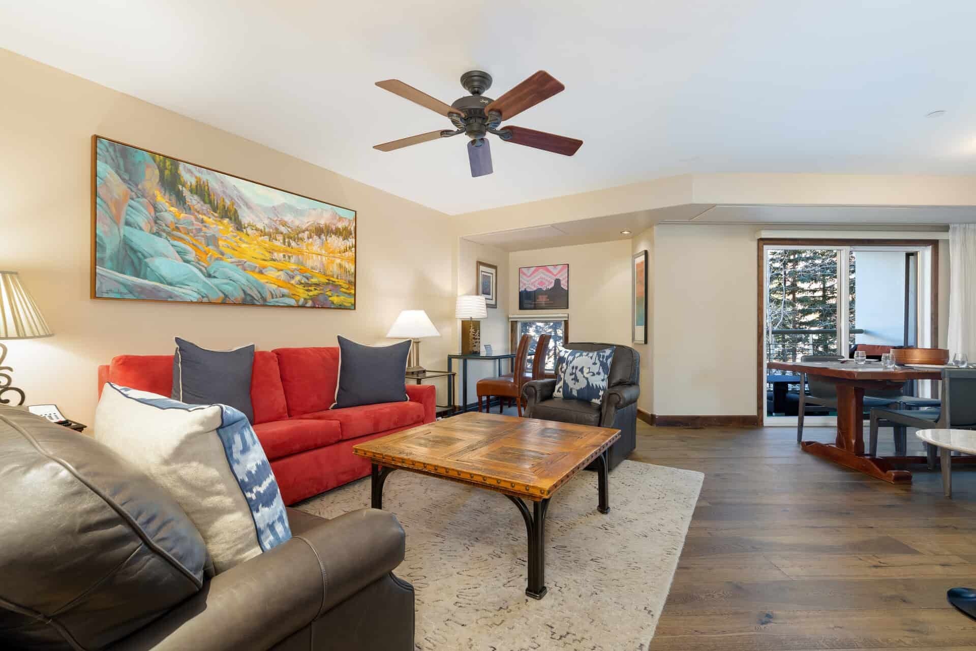 A living room with a red sofa, a brown leather couch, a wooden coffee table, and a ceiling fan.