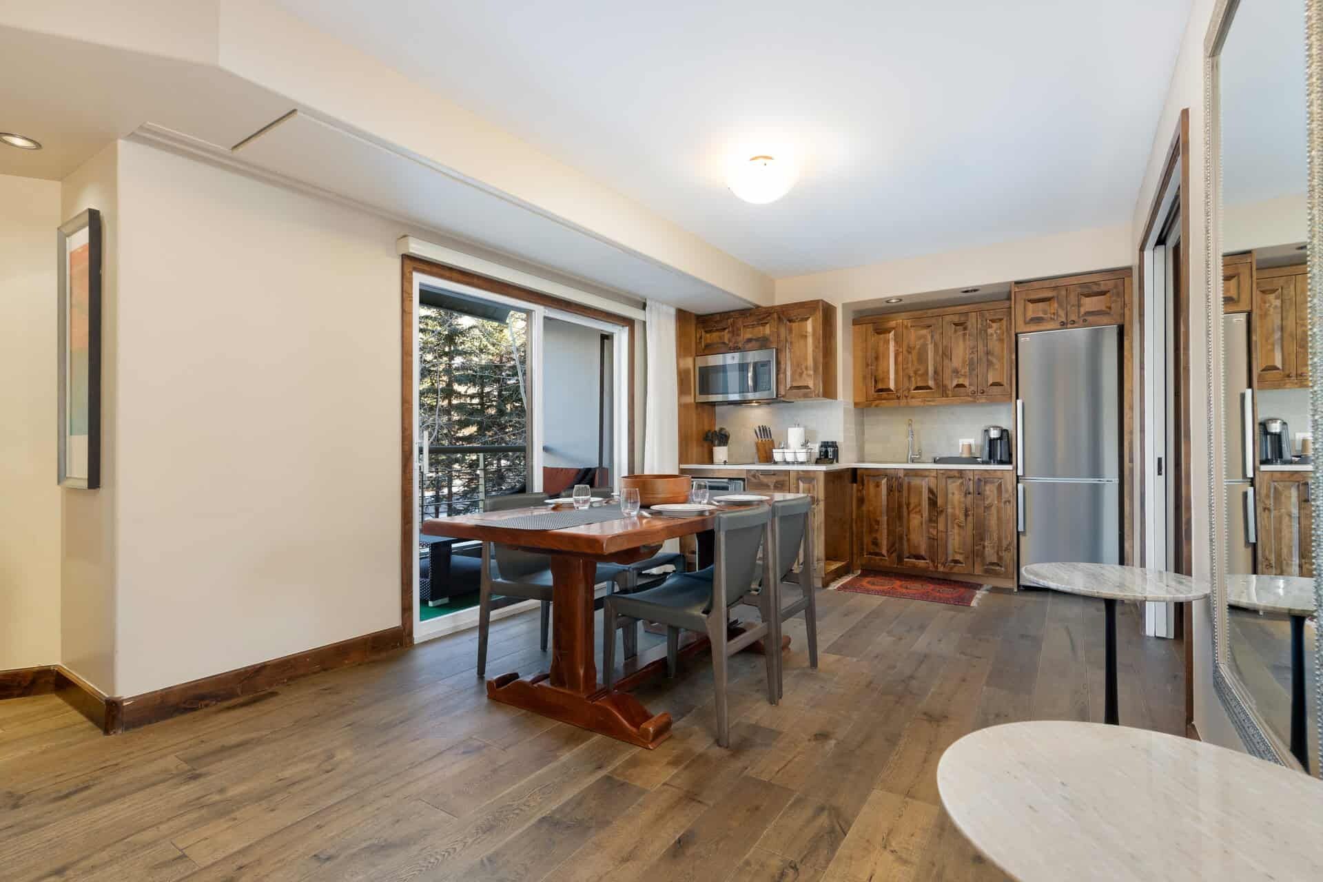 A modern kitchen with wooden cabinets, a dining area with a table and chairs, and a large refrigerator.