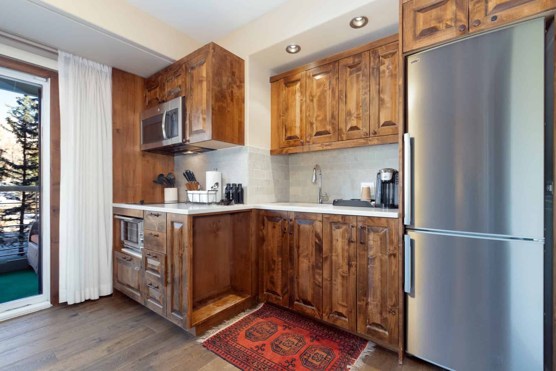 A kitchen with wooden cabinets, stainless steel appliances, and a view of a snowy landscape through a sliding door.