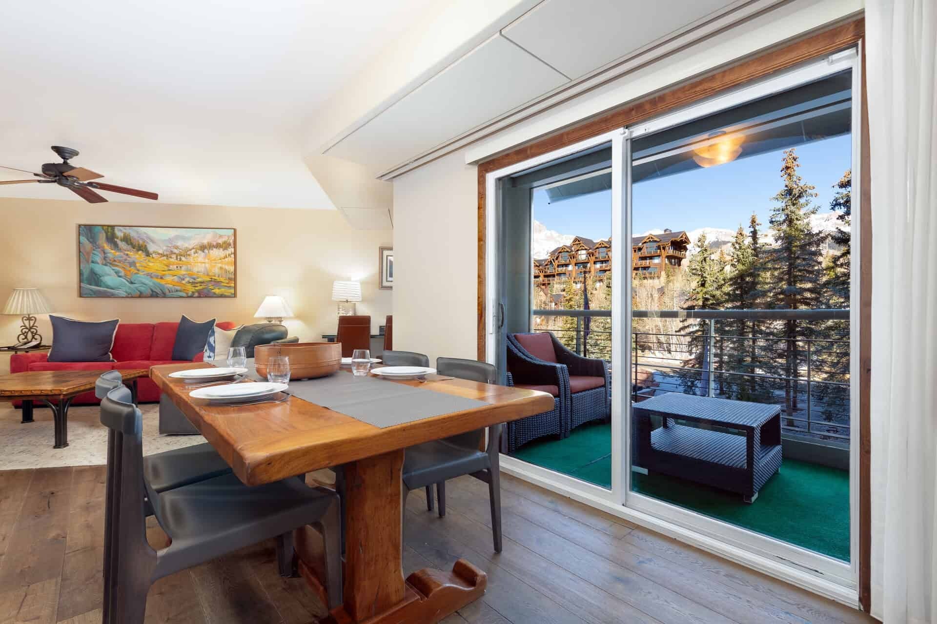 A spacious living area with a dining table, sofas, and a large sliding glass door leading to a balcony with a mountain view.