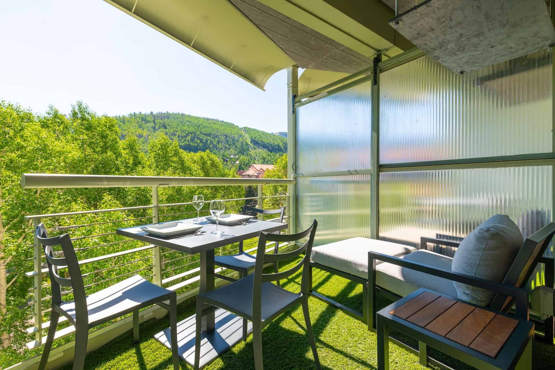Een balkon met een eettafel gedekt voor twee personen, stoelen en een bank met kussens.