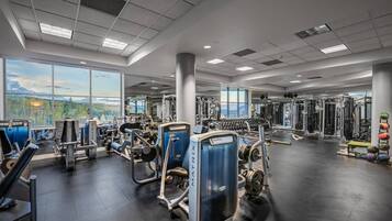 A gym with various exercise equipment, large windows, and a view of the outdoors.