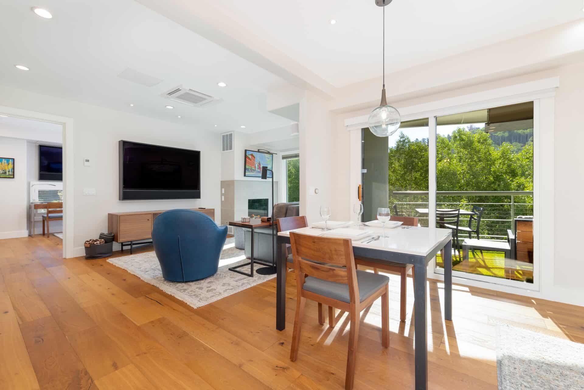 Una sala moderna con un televisor de pantalla plana, un comedor con mesa y sillas, y un balcón con mobiliario exterior.