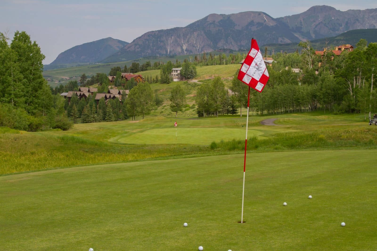 A golf course with a flagstick, a flag, and a distant mountain range.