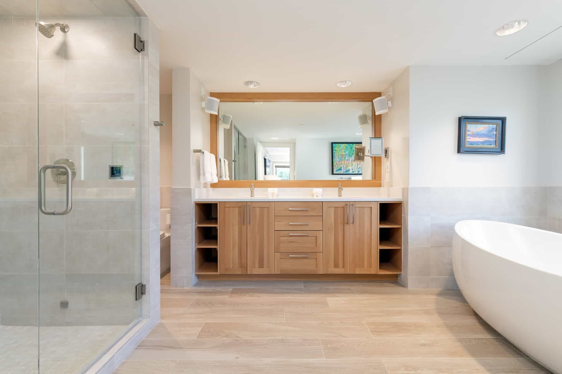 Ein modernes Badezimmer mit barrierefreier Dusche, einer freistehenden Badewanne und einem großen Spiegel über dem Waschtisch.