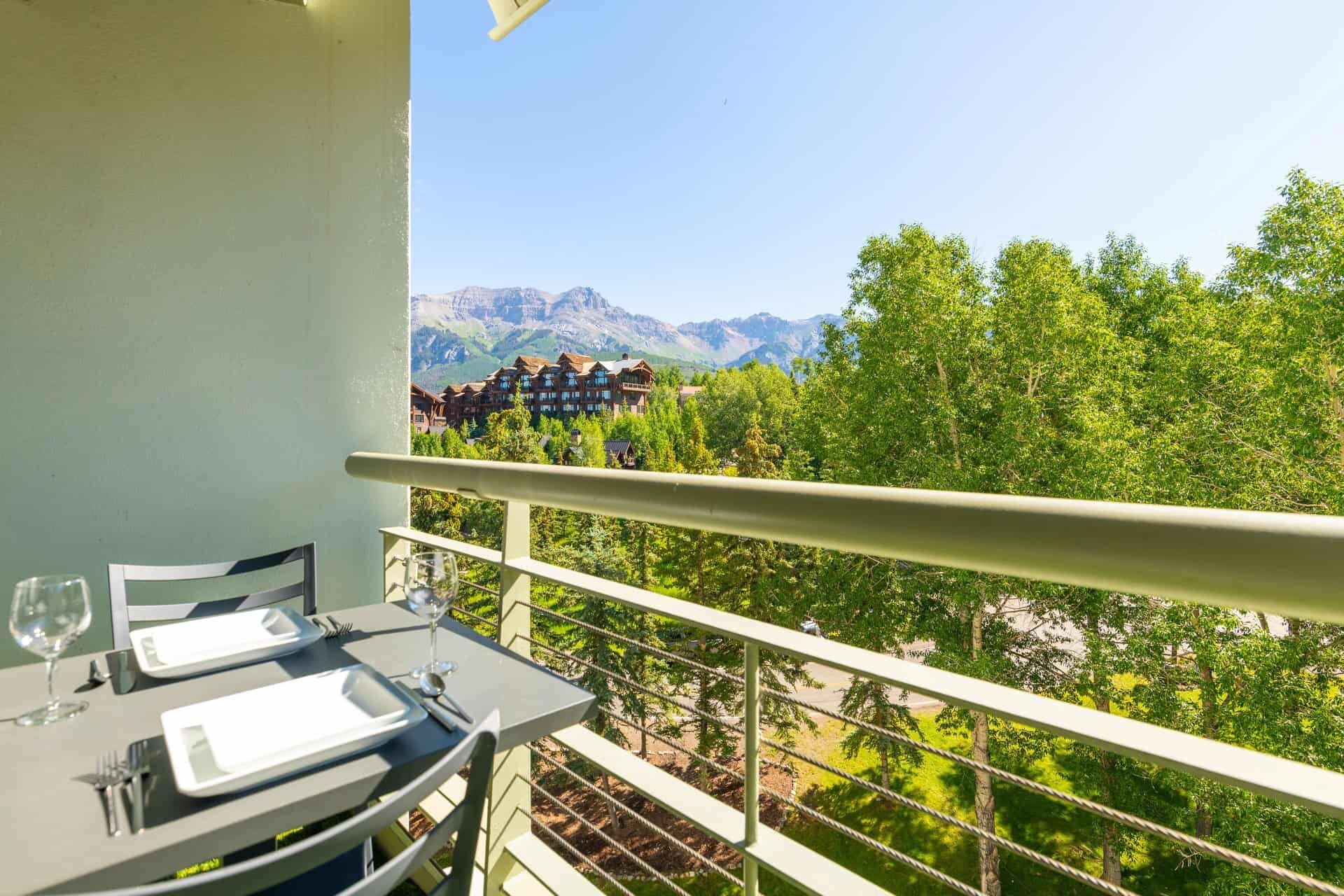 A balcony with a table set for two, overlooking a mountainous landscape with buildings.