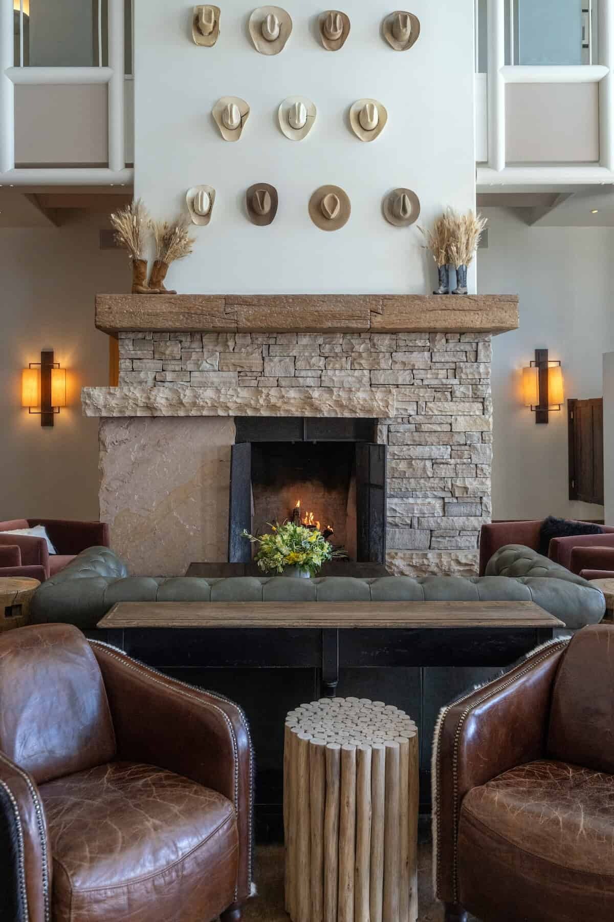 A stone fireplace with a mantel, surrounded by leather sofas and a wooden stool.
