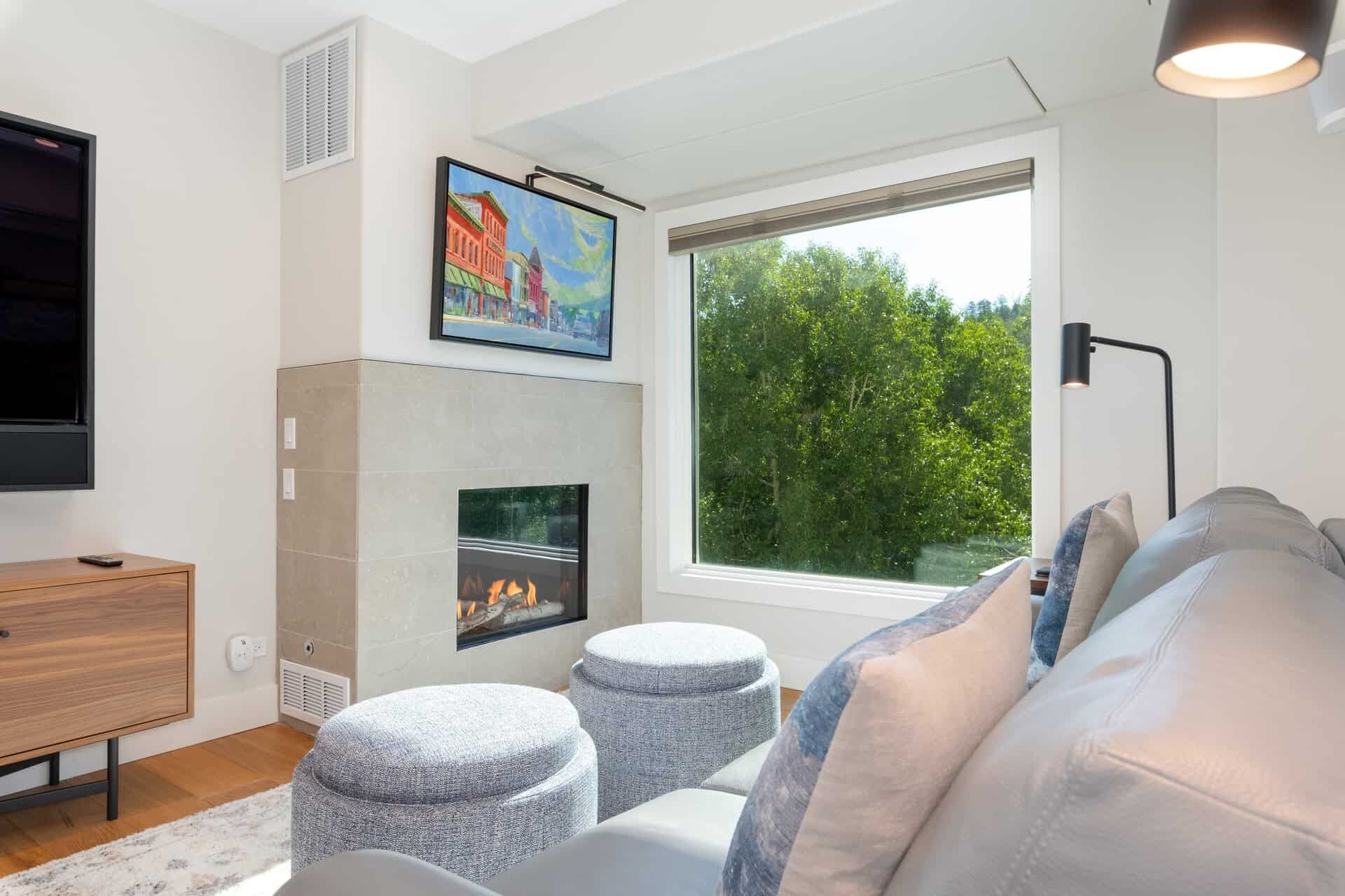 Una sala de estar moderna con chimenea, televisor y un ventanal con vista a árboles.