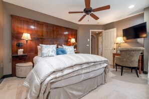 Un dormitorio con una cama grande, ventilador de techo, televisor y una silla.