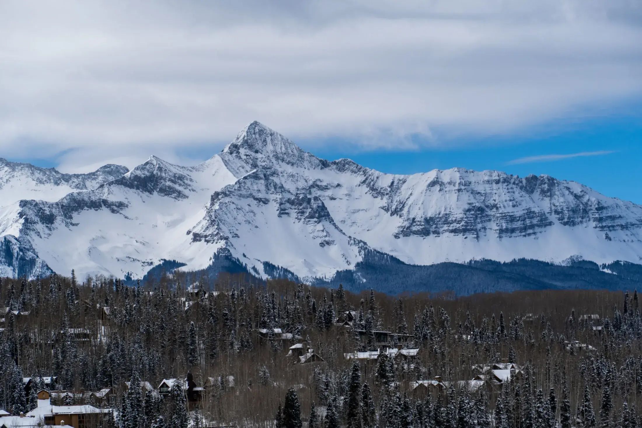 A mountain landscape with snow-covered peaks and a forested valley with buildings.