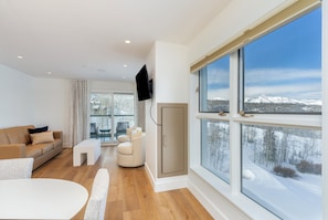 A modern living room with a sofa, a coffee table, and a TV mounted on the wall. - Ski-In/Ski-Out 1BR Suite w/ Balcony Views + Pools (Mountain Village)