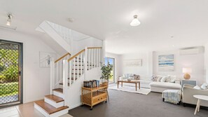 A spacious living area with a staircase, a sofa set, a coffee table, and a bookshelf.