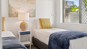 A bedroom with two beds, a nightstand, a lamp, and a window with a view.