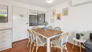 A dining area with a wooden table and wicker chairs, a white cabinet, and a window with blinds.