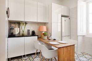 A modern kitchen with white cabinets, a wooden countertop, a white chair, and a built-in refrigerator. - Graça Retreat | Spacious 2BR in Lisbon (Lisbon)