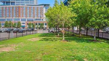 A grassy area with trees and a fence, a parking lot with cars, and a building with multiple floors and windows.