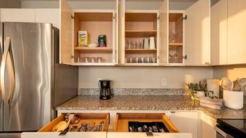 A kitchen with a stainless steel refrigerator, open cabinets, a coffee maker, and a drawer with kitchen tools.