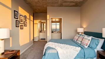 A bedroom with a bed, bedside lamps, a nightstand, a dresser, and a bathroom visible through an open door.