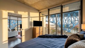 A modern bedroom with a large bed, a television, and a view of a blue bridge outside. - Spacious 3-bedroom apartment with AC in soothing Cleveland (Cleveland)