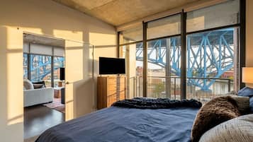 A modern bedroom with a large bed, a television, and a view of a blue bridge outside.