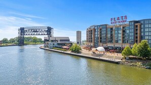 En utsikt över vattnet med en bro, en modern byggnad med en skylt som visar texten ”FIAT’S EAST BANK” och ett område med restauranger och uteservering.
