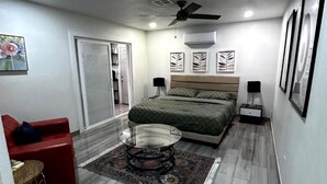 Un dormitorio con cama, sofá rojo, mesa de centro de vidrio y ventilador de techo.