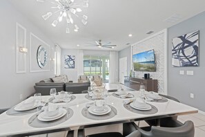 A modern dining area with a large table set for a meal, a ceiling fan, and a TV on the wall. - Luxury 7BR Disney Home • Pool Spa • Game Room -  Resort Windsor Island (Four Corners)
