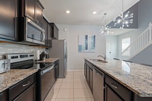 A modern kitchen with dark cabinetry, a stainless steel refrigerator, and a granite countertop. - Luxury 7BR Disney Home • Pool Spa • Game Room -  Resort Windsor Island (Four Corners)